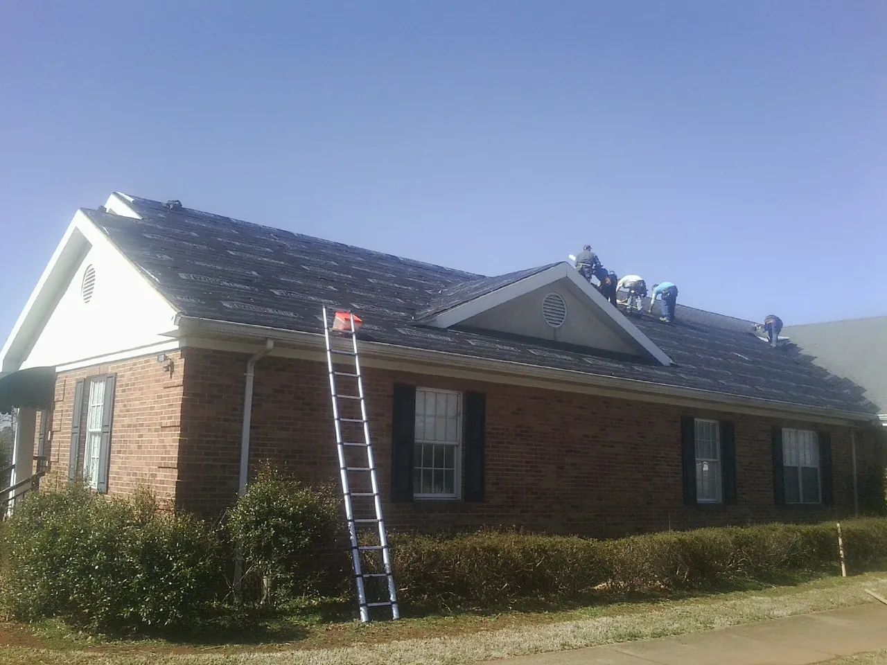 Crew tearing shingles off a brick ranch roof with a ladder set — Emergency Roof Repair work by our crew in Port Republic