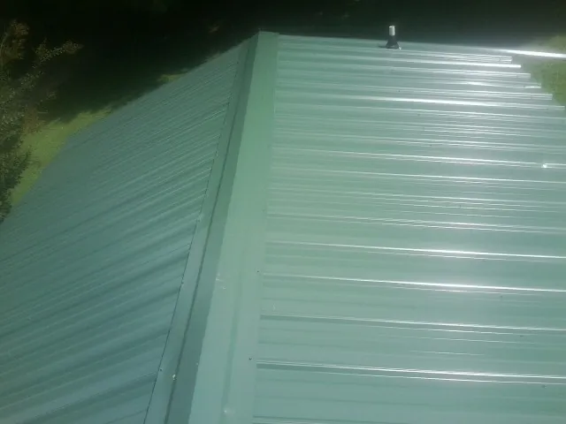 New green metal panels meeting at the ridge of a roof — Flat Roof Repair work by our crew in Port Republic