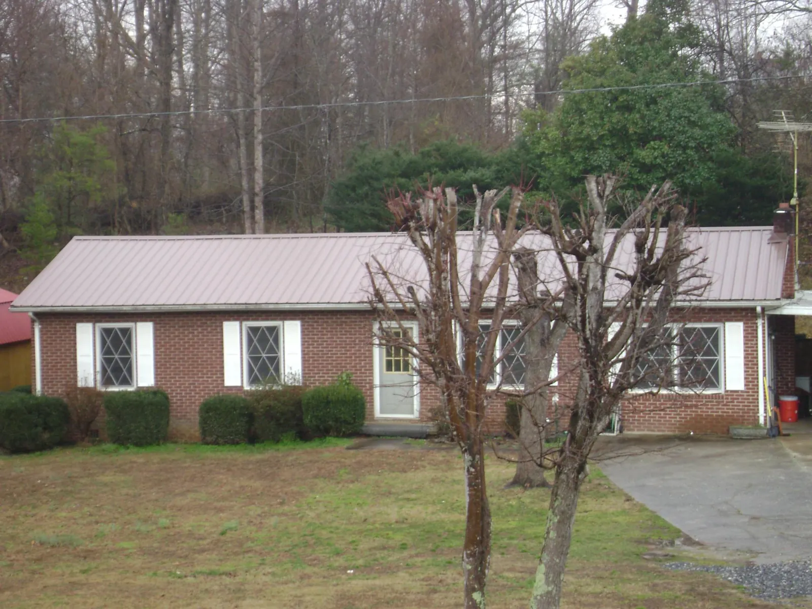 Mauve metal roof on a brick ranch home behind bare trees in Port Republic